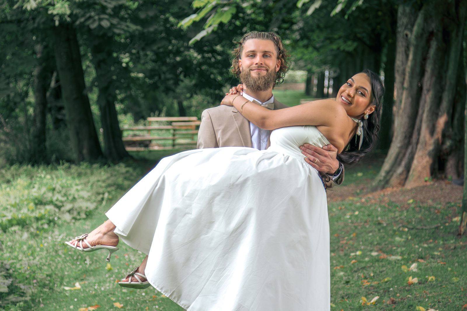 Le marié porte la mariée, vue large sur l'allée du parc