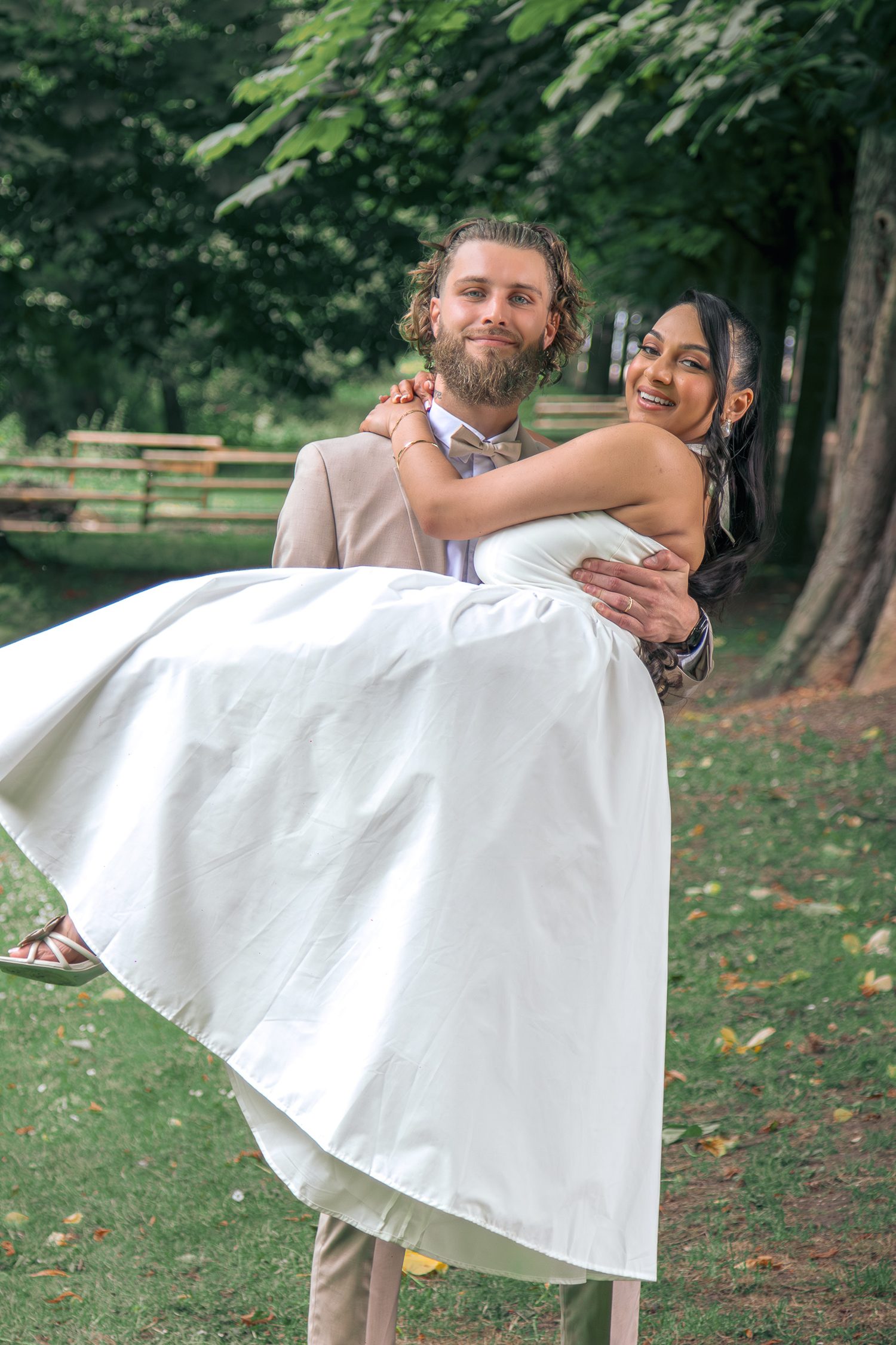 Le marié porte la mariée dans ses bras au milieu du parc
